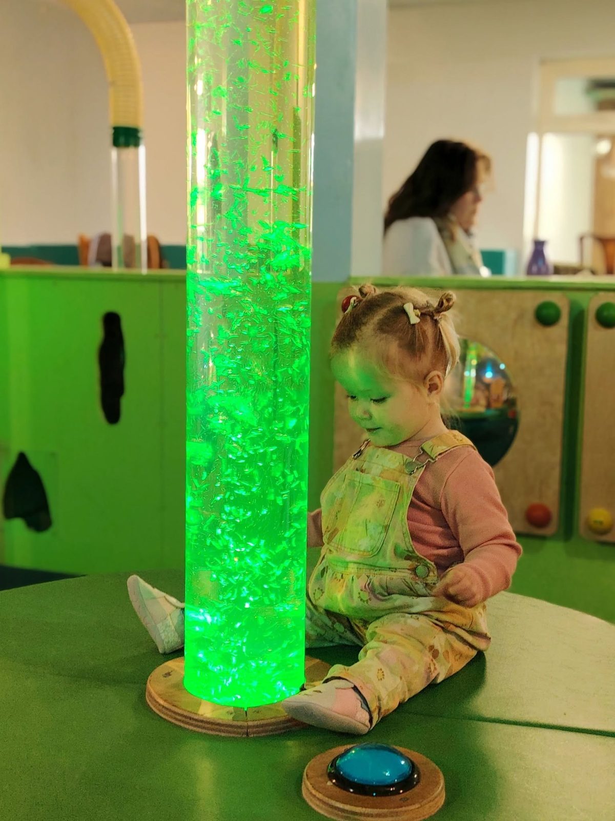 A toddler sitting beside the glowing green bubble tube